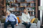 Senior couple arguing while wife is on the phone with gray divorce attorney.